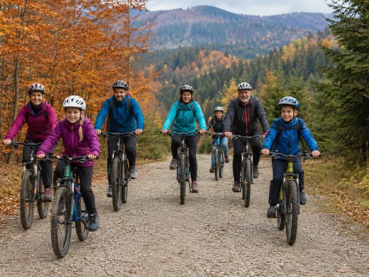 Dzieci, dorośli i starsi uczestnicy jadący rowerami MTB szeroką leśną drogą